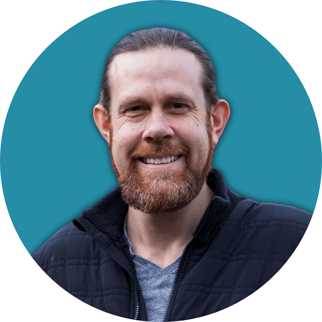 Joel Tarbutton with a beard and long hair, wearing a black jacket, set against a teal background.