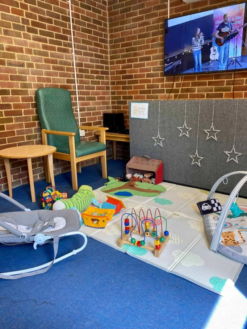 Children's play area with toys, a rocking chair, a small table, and a TV showing people singing and playing guitar.