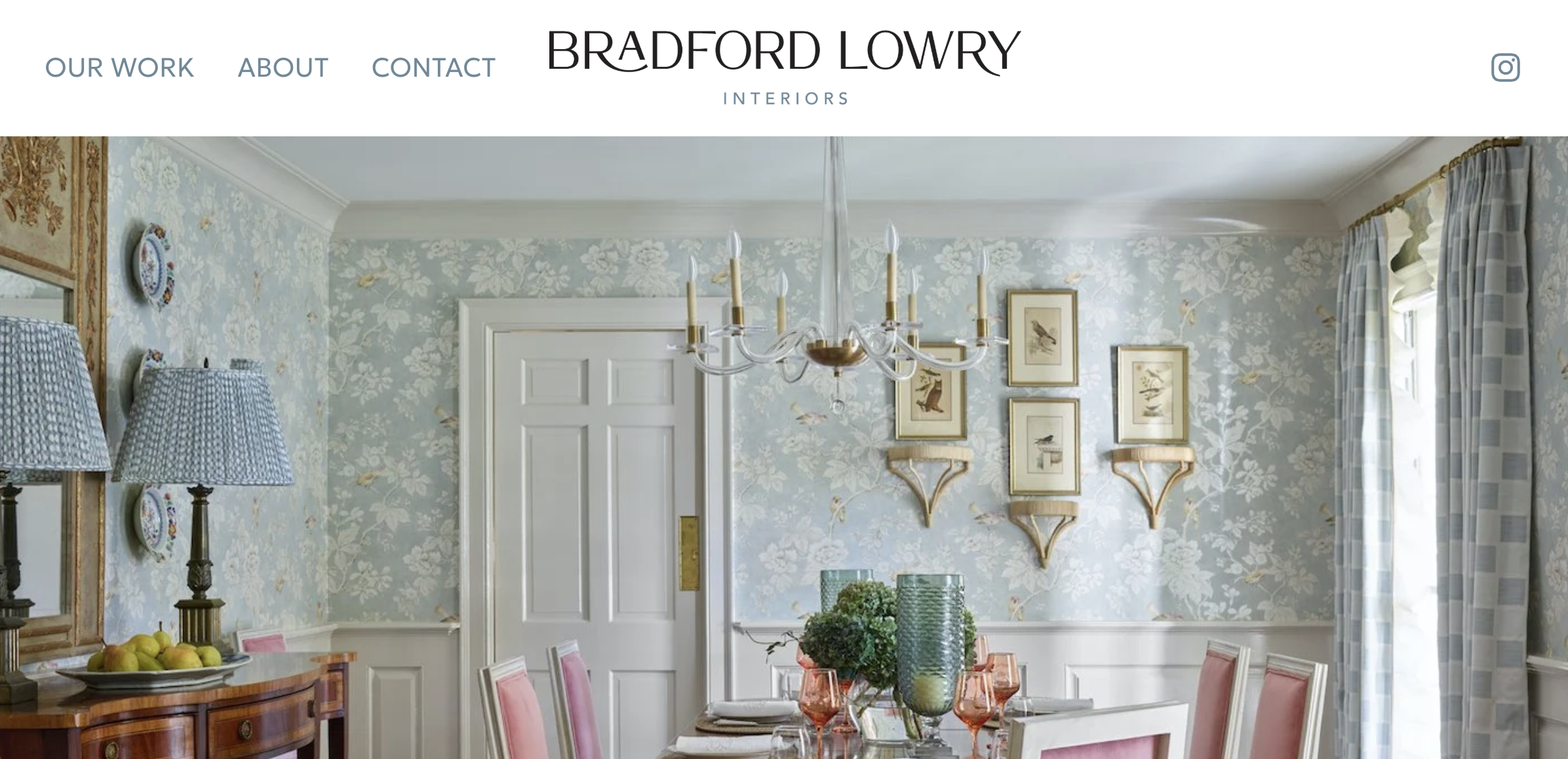 A screenshot of a website showing the interior of a dining room with floral wallpaper, framed bird prints, a white door, a chandelier, a side table with lamps and fruit bowl, and a window with checkered curtains.