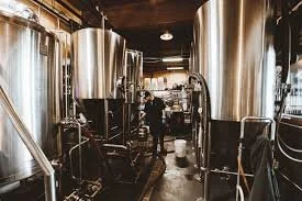 Inside a brewery with large stainless steel brewing tanks and a person working.