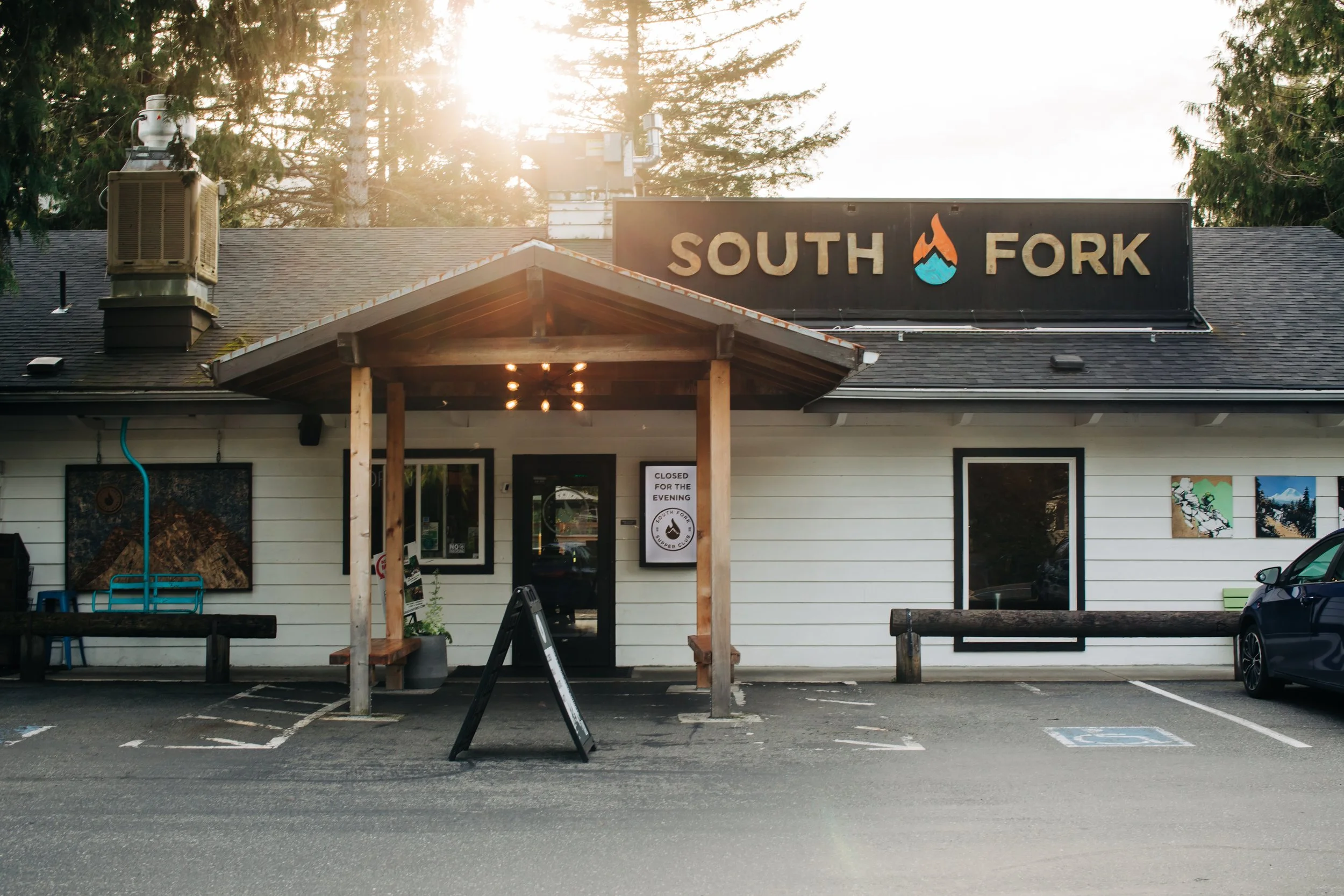 Front of a restaurant called South Fork, with a sign above and a small covered porch. The restaurant appears to be closed for the evening, with a sign on the door stating so. The parking lot in front has marked spaces, including a handicap space.