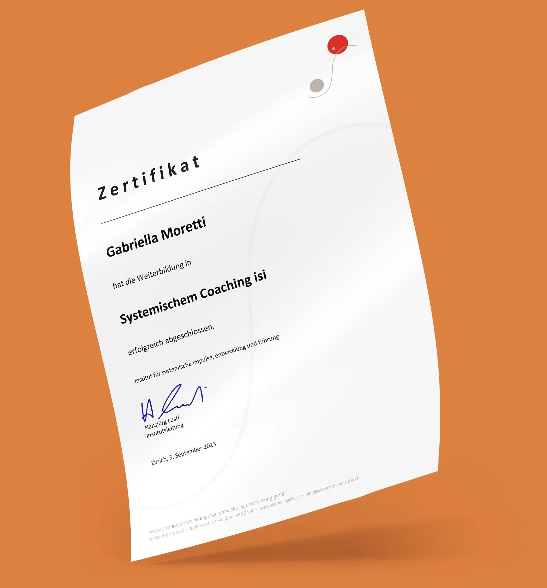 Ein Zertifikat von Gabriella Moretti, unterschrieben von Hansjürg Lusti, auf weißem Papier vor braunem Hintergrund. Der Text ist in Deutsch und bezieht sich auf eine Weiterbildung in systemischem Coaching.
