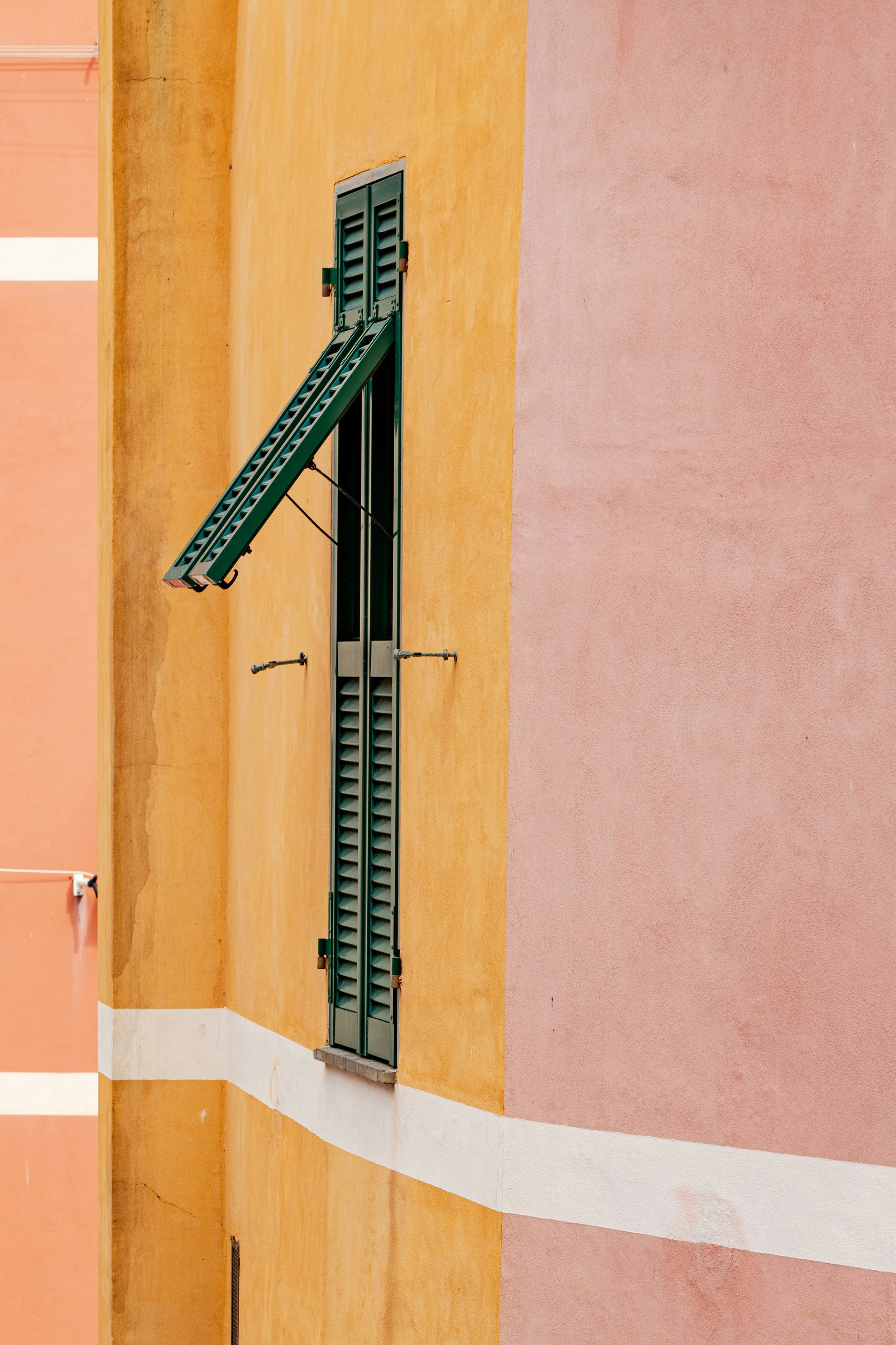 Blick auf ein Fenster mit grünen Shutter an einem gelben und rosa Wand im Freien.