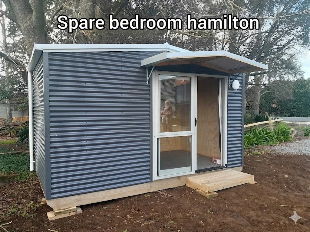 A small, metal shed with a glass door and a small wooden ramp in a backyard, labeled as 'Spare bedroom hamilton'.
