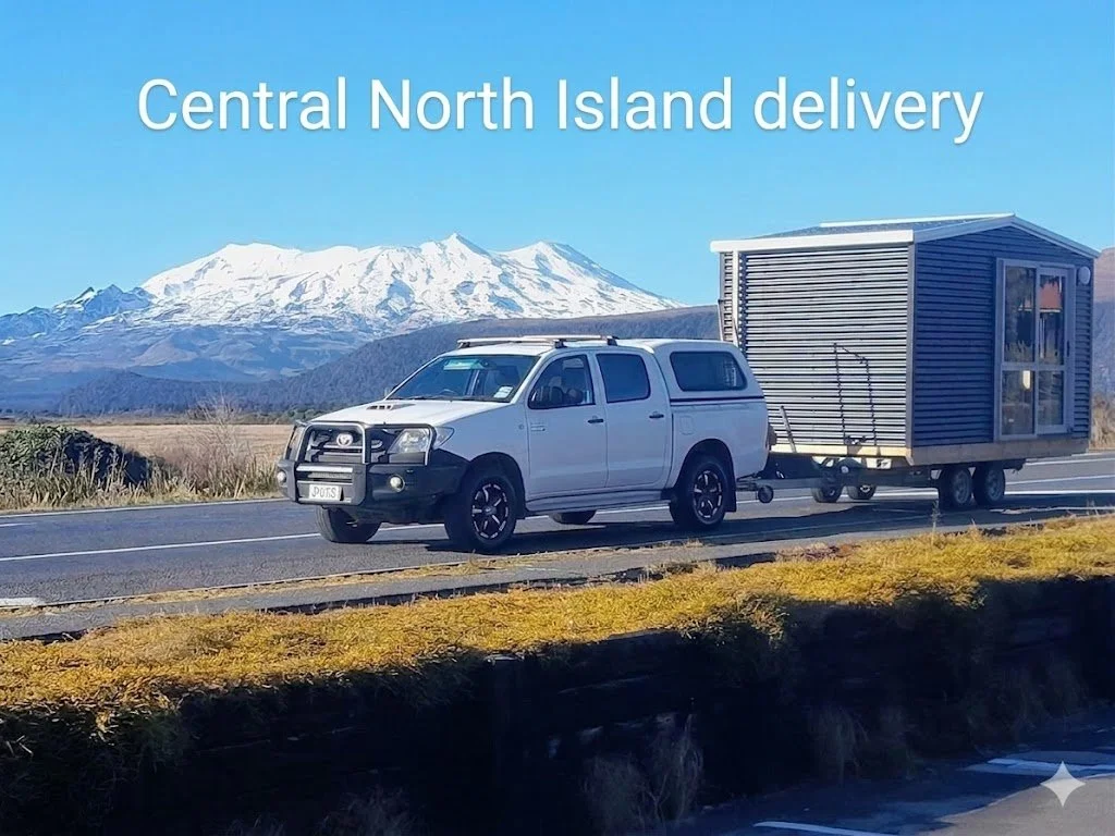 A white pickup truck towing a tiny house on wheels with a mountain and clear blue sky in the background, with the text 'Central North Island delivery' on the image.