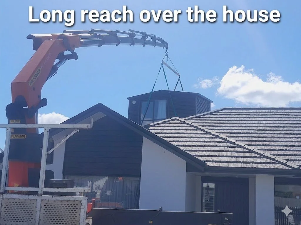 A crane lifting a small black house over a larger residential building with a sloped tiled roof.