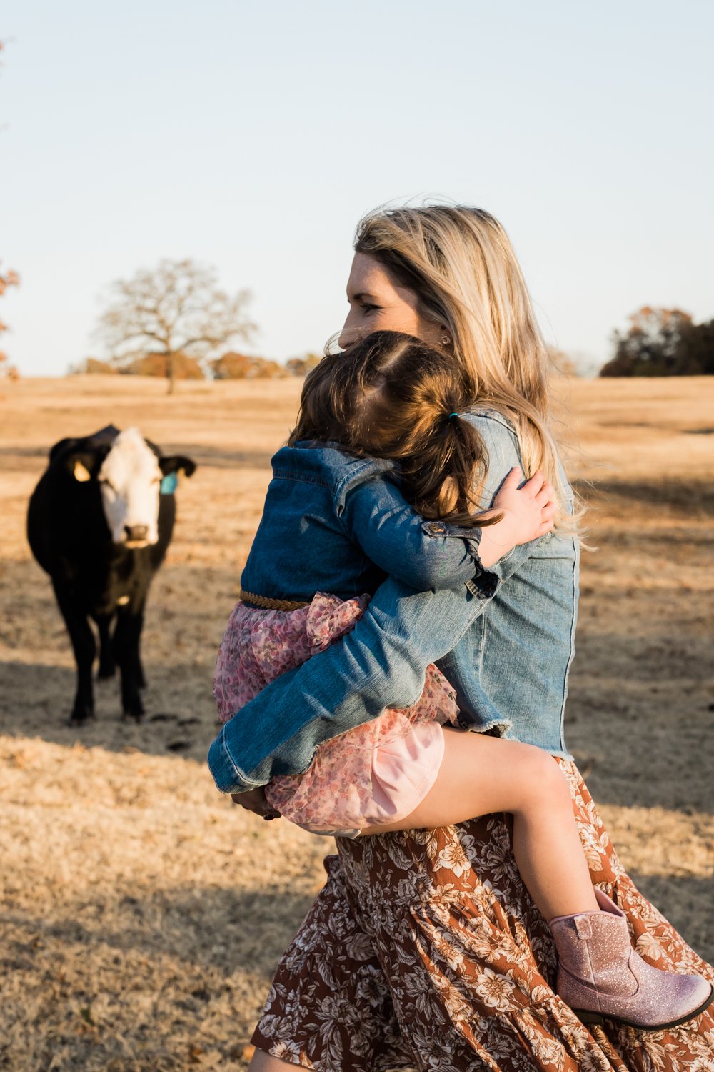 Mom holding little girl on farm with cow