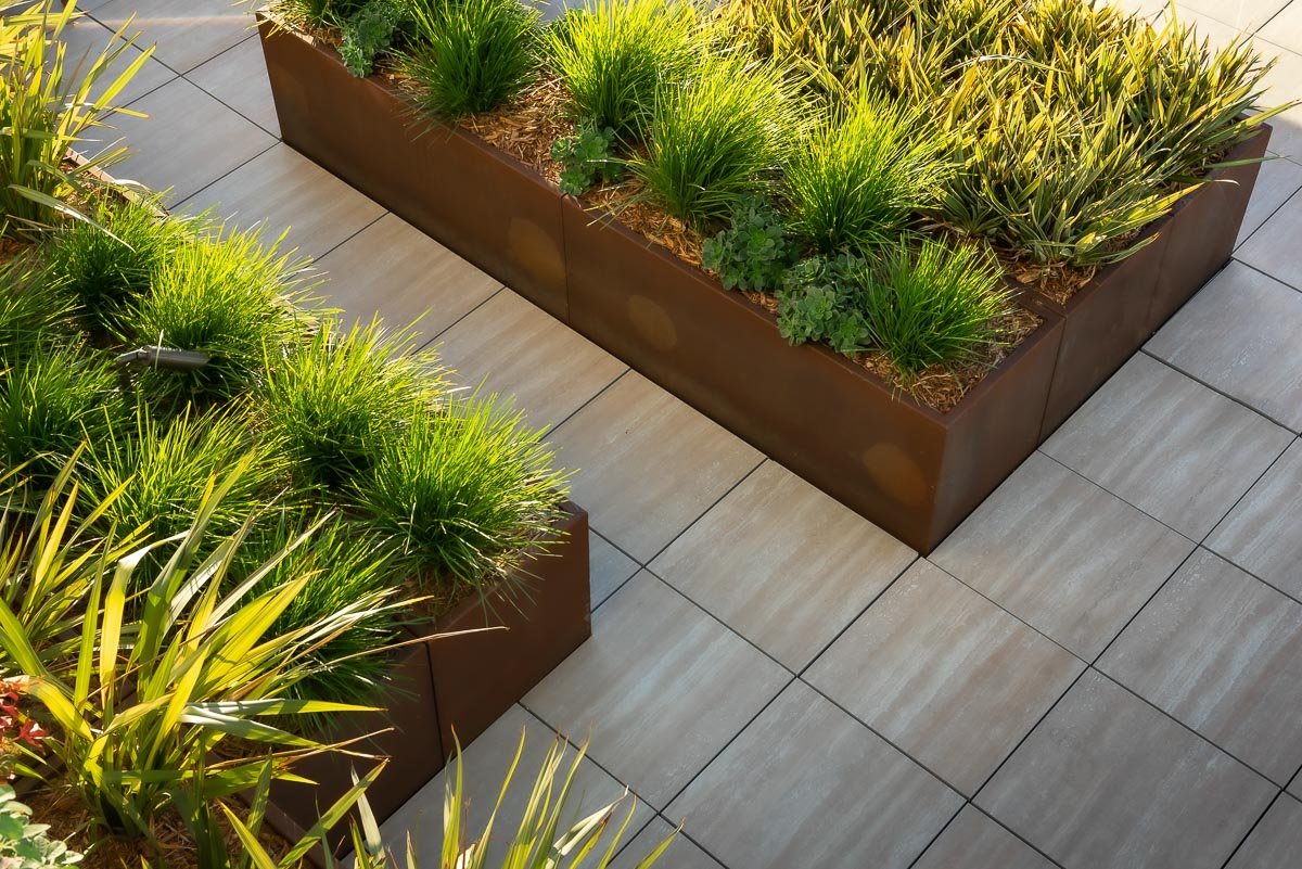 abstract view of metal planters filled with lush plants, and stone pavers around the planters