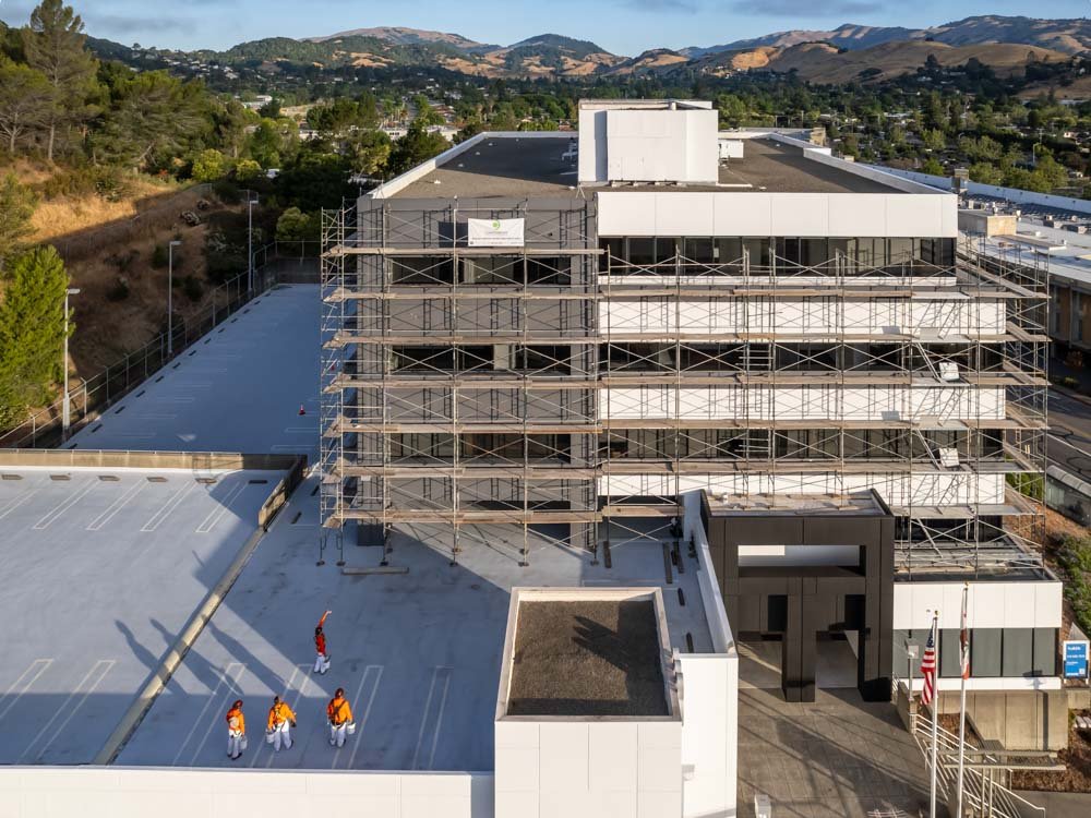 Drone view of an office building with scaffolding and a construction crew on the ground.