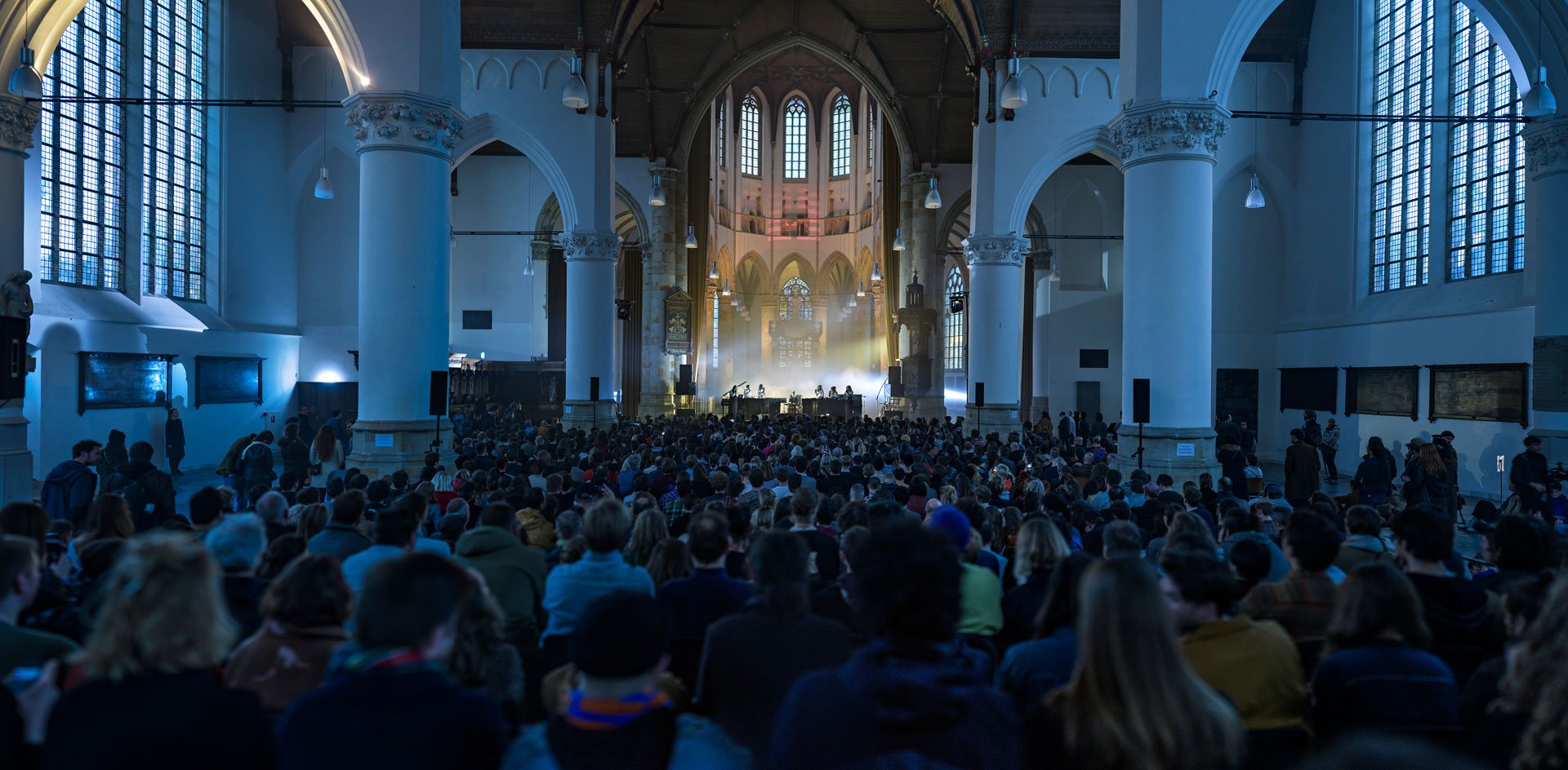 Church interior with live performance, audience seated, large arched windows.