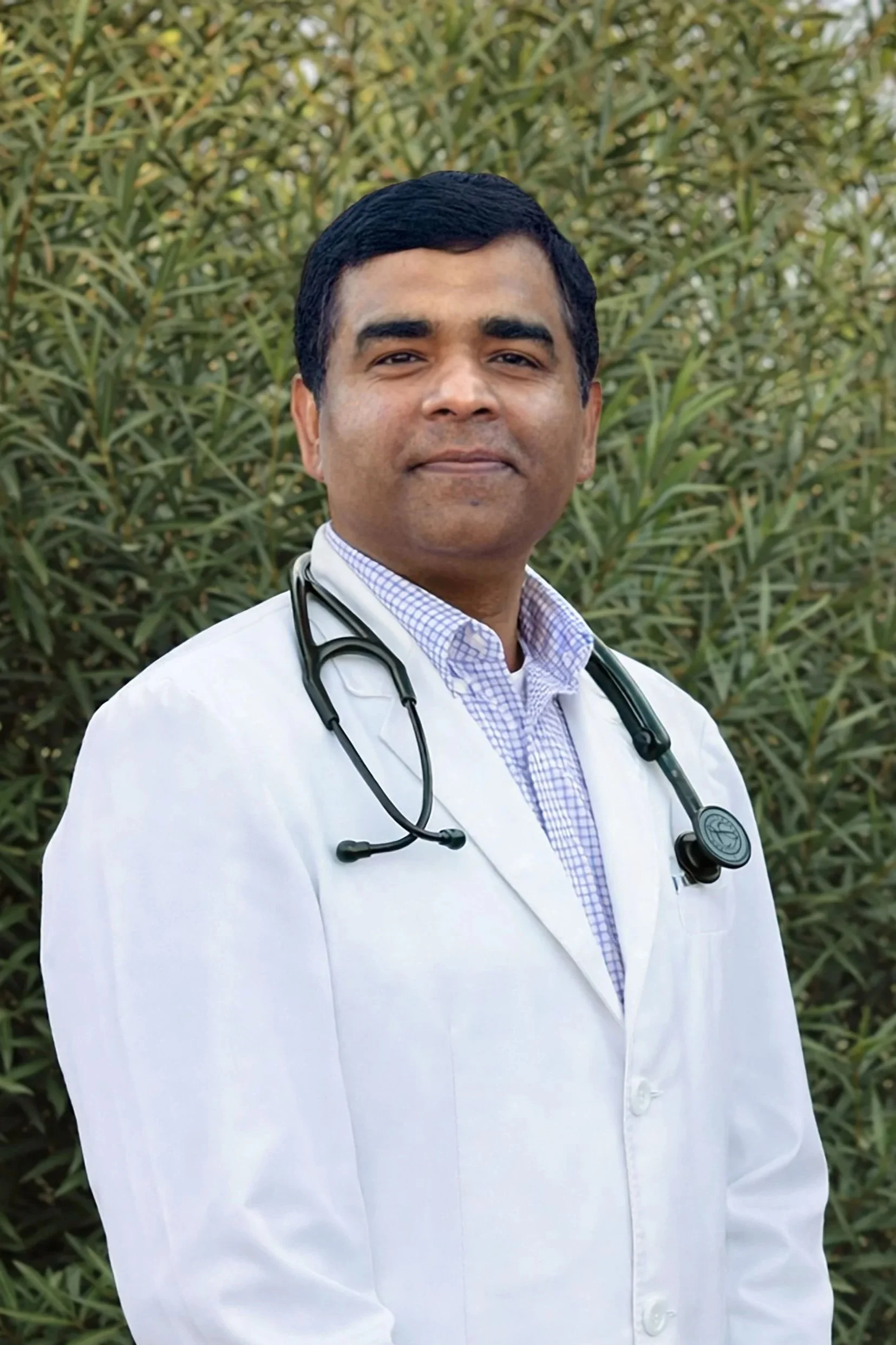 Man in a white lab coat and blue checkered shirt smiling
