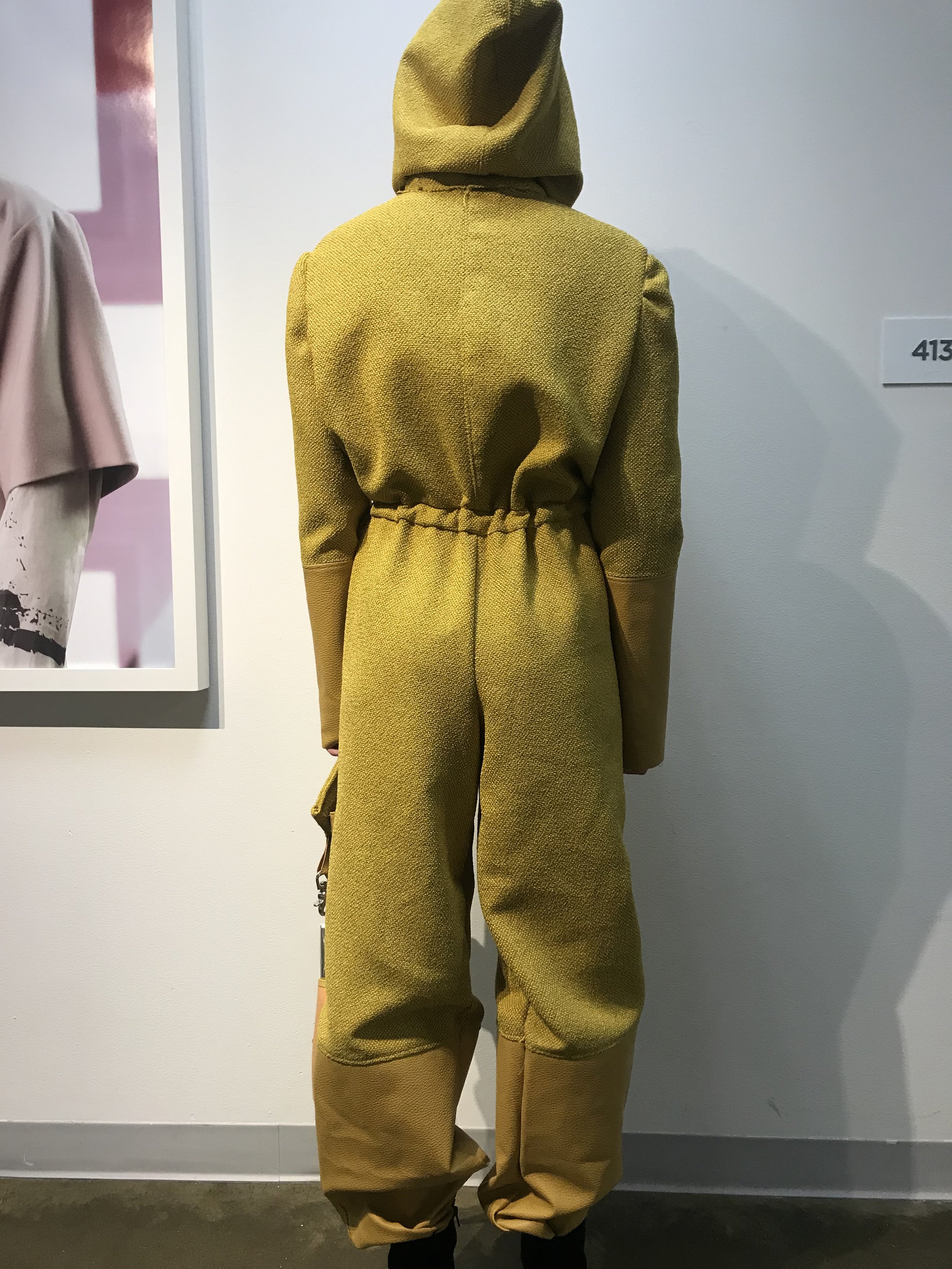 Back view of a woman wearing a yellow hoodie and matching yellow pants in an art gallery.