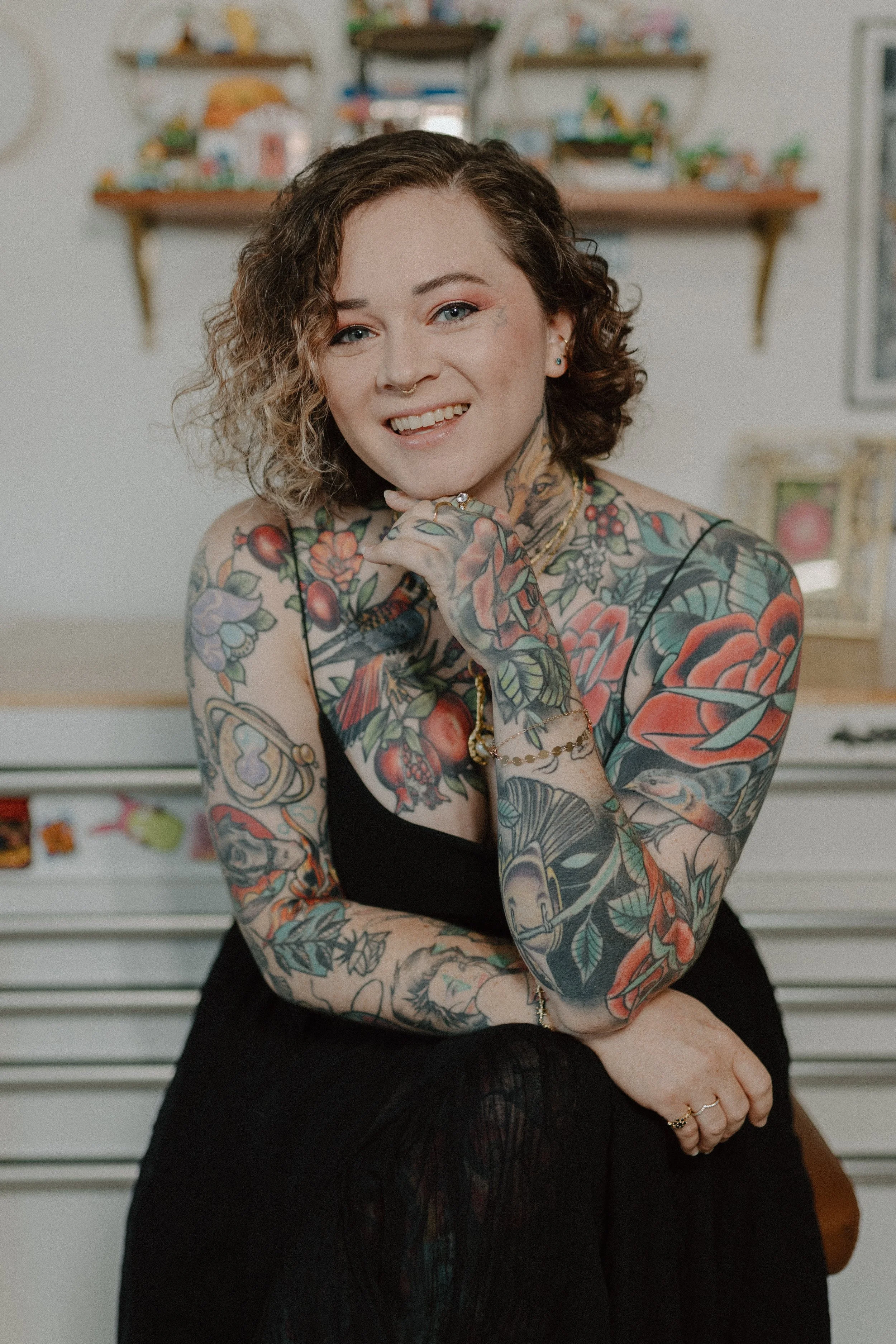 Photo of the artist, a woman with brown curly hair and tattoos