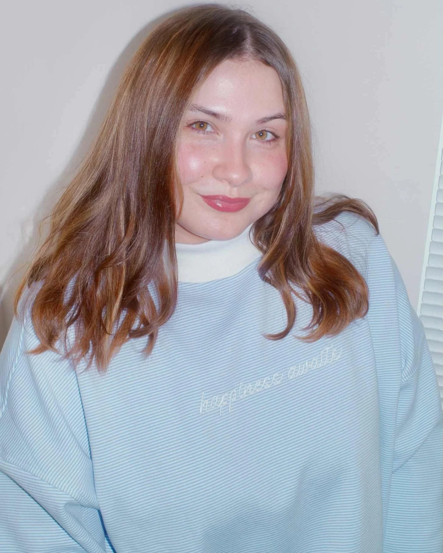 GIRL WEARING BLUE AND WHITE STRIPED MOCKNECK WITH WHITE EMBROIDERED TEXT THAT READS 'HAPPINESS AWAITS'
