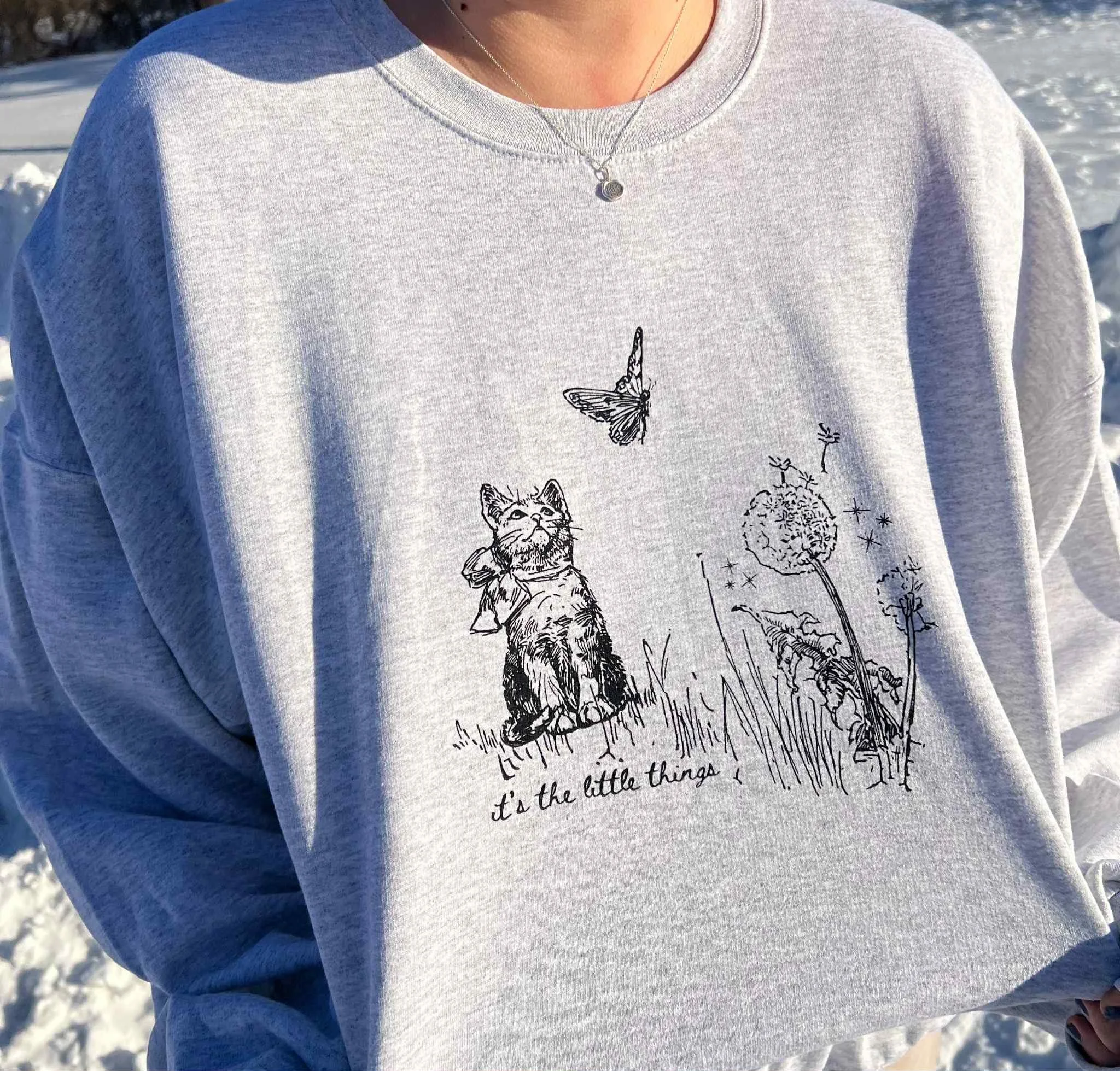 ASH GRAY SWEATSHIRT WITH ILLUSTRATION OF CAT AND BUTTERFLY WITH TEXT THAT READS 'ITS THE LITTLE THINGS' BELOW