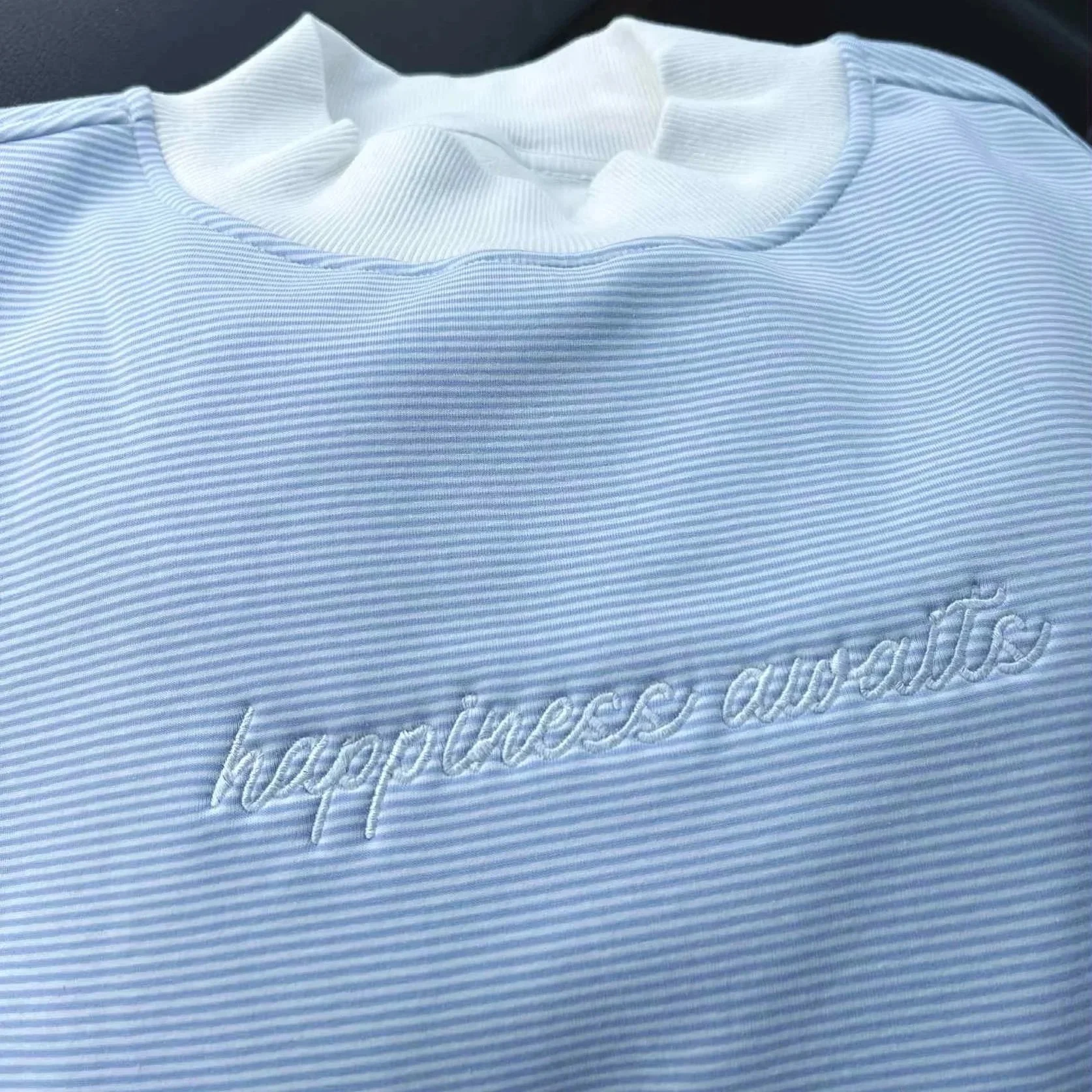 BLUE AND WHITE STRIPED MOCKNECK WITH WHITE EMBROIDERED TEXT THAT READS 'HAPPINESS AWAITS'