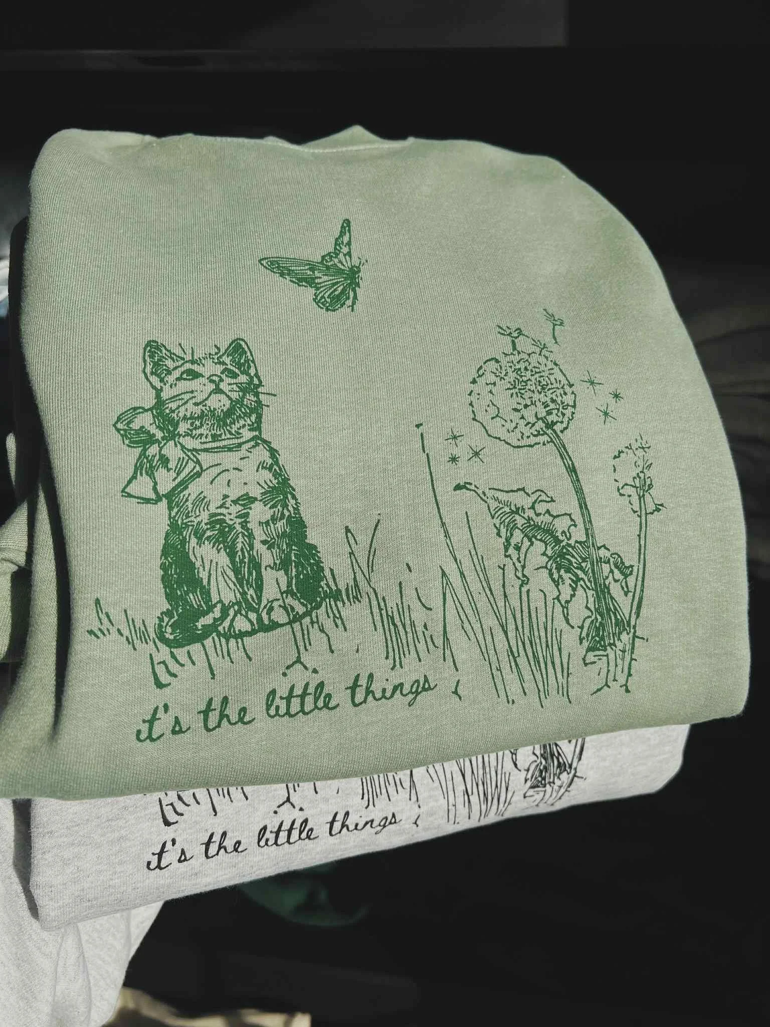 SAGE GREEN SWEATSHIRT WITH ILLUSTRATION OF CAT AND BUTTERFLY WITH TEXT THAT READS 'ITS THE LITTLE THINGS' BELOW