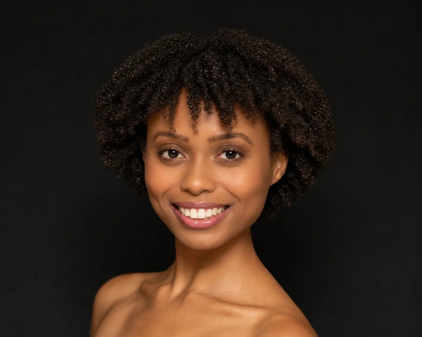 Portrait of a smiling young woman with dark hair in a bun against a plain white background.
