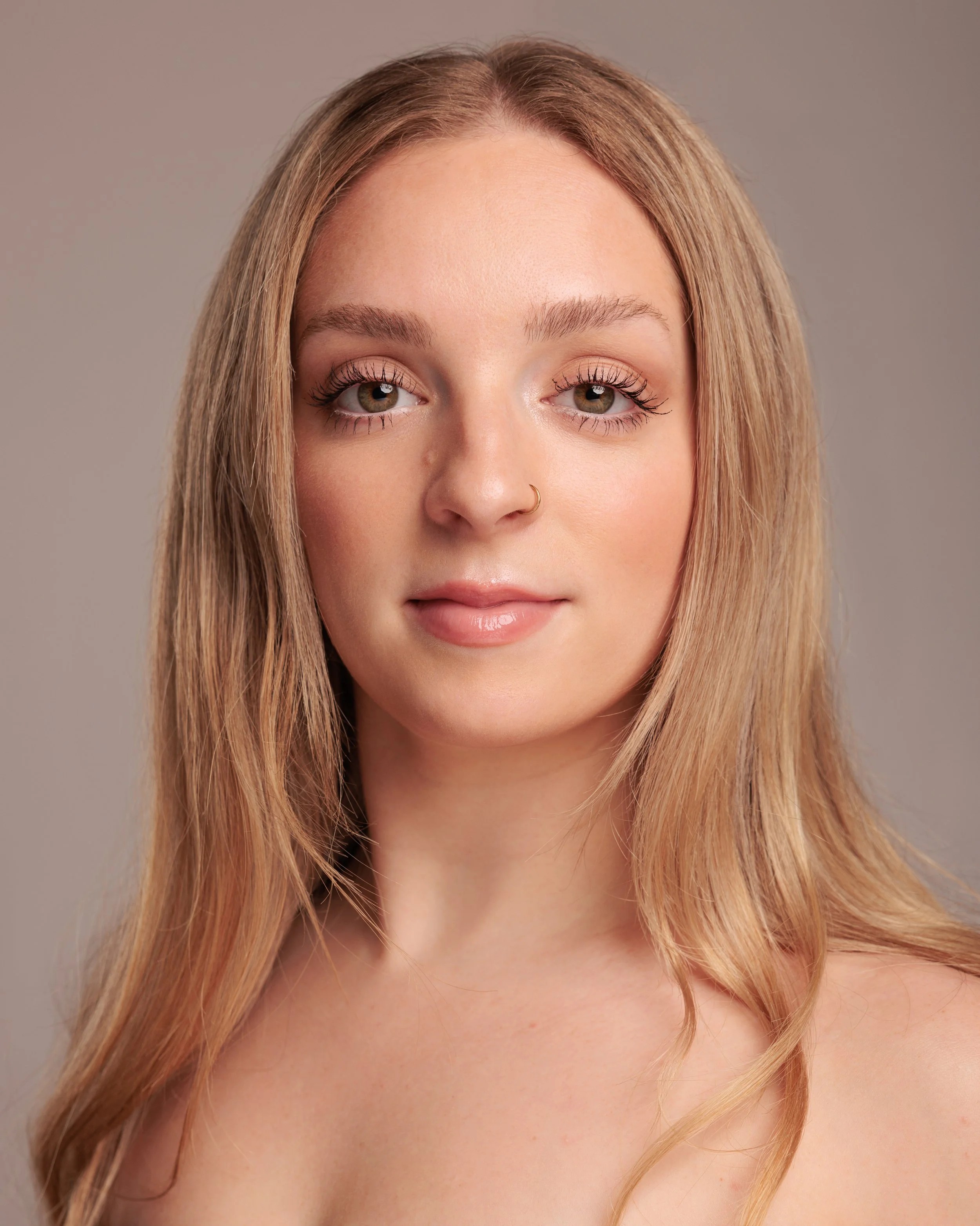 A woman with wavy light brown hair and fair skin against a dark gray background.
