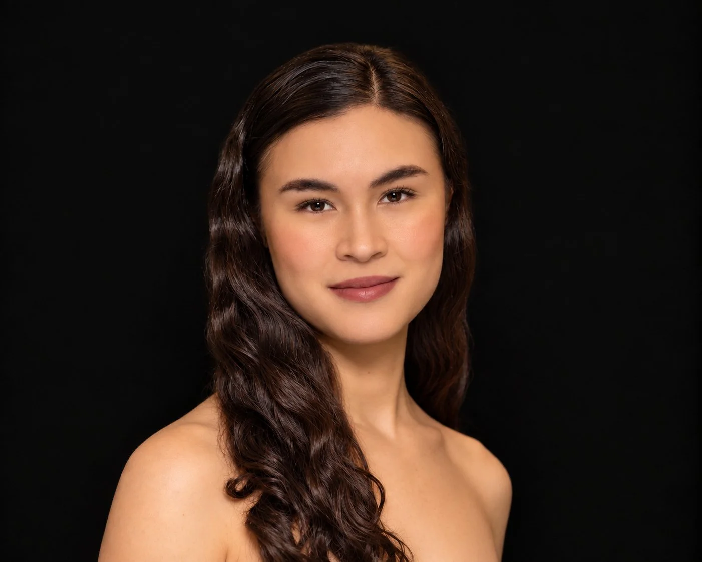 A smiling young woman with long dark hair against a dark gray background.