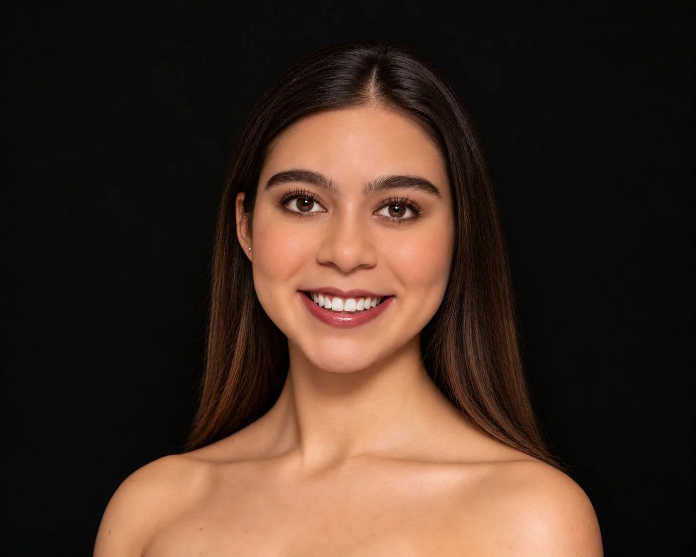 A young woman with long brown hair smiling at the camera, wearing a black spaghetti strap top.