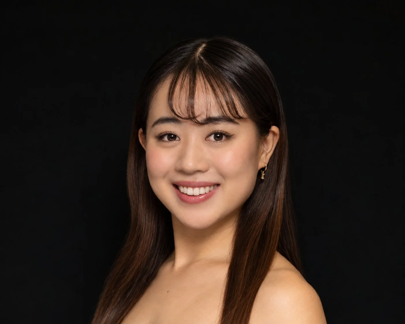 Close-up of a woman with long black hair, light skin, and subtle makeup, wearing a black spaghetti strap top, against a white background.
