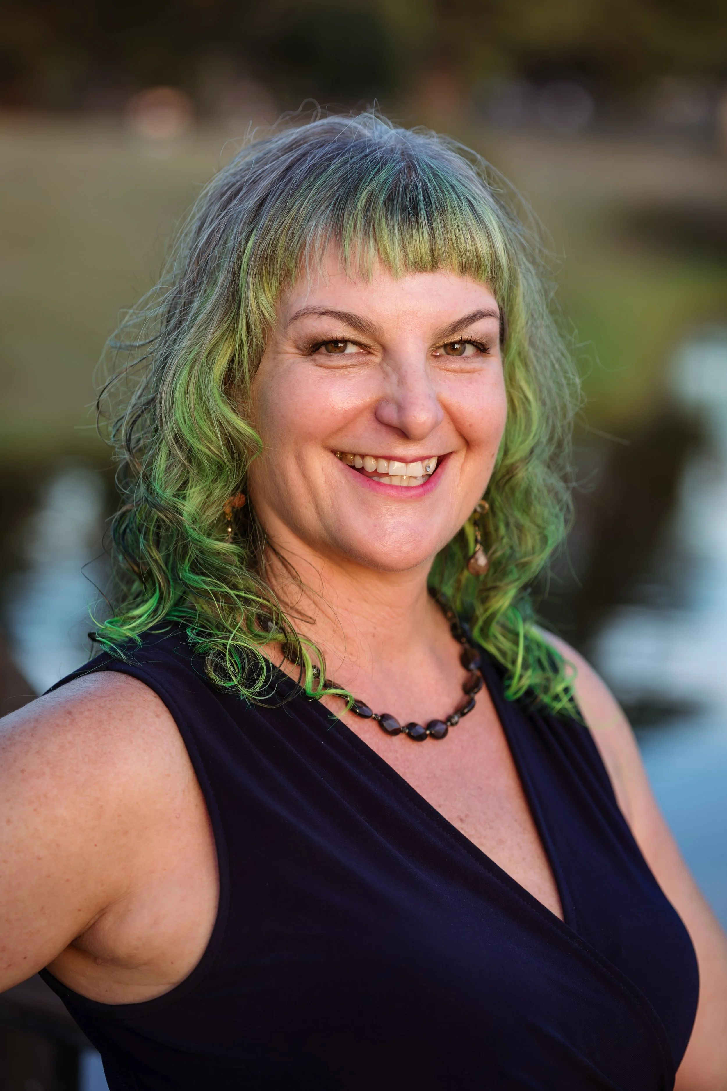 Acupuncturist smiling, wearing a blazer, standing in a room with hexagonal shelves and a wooden counter.