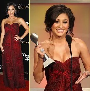 Francia Resia in a red strapless gown standing on the red carpet and another woman in a similar gown holding an award while speaking at a microphone.