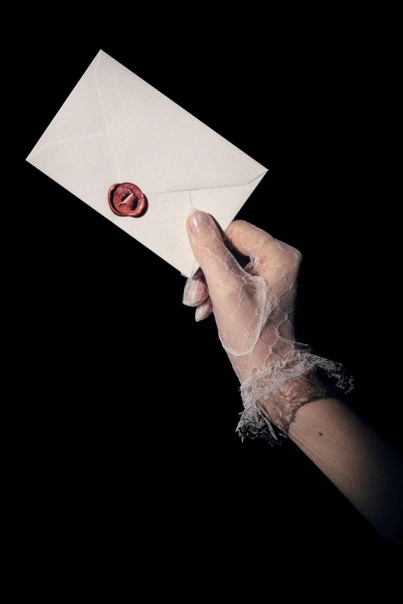 A hand with lace gloves holding a white envelope sealed with a red wax seal against a black background.