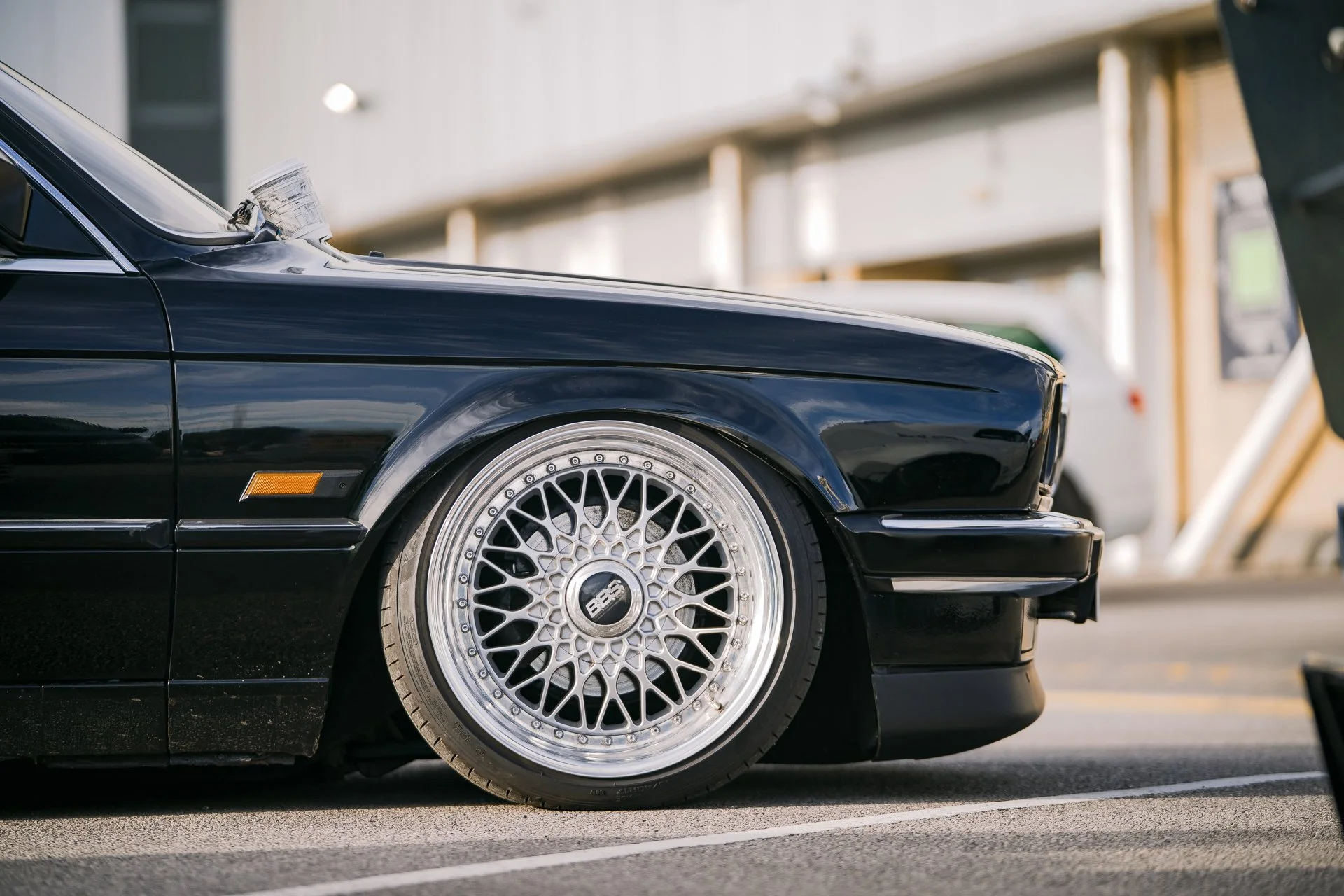 Close-up of a black classic car with custom silver BBS wheels parked outdoors.