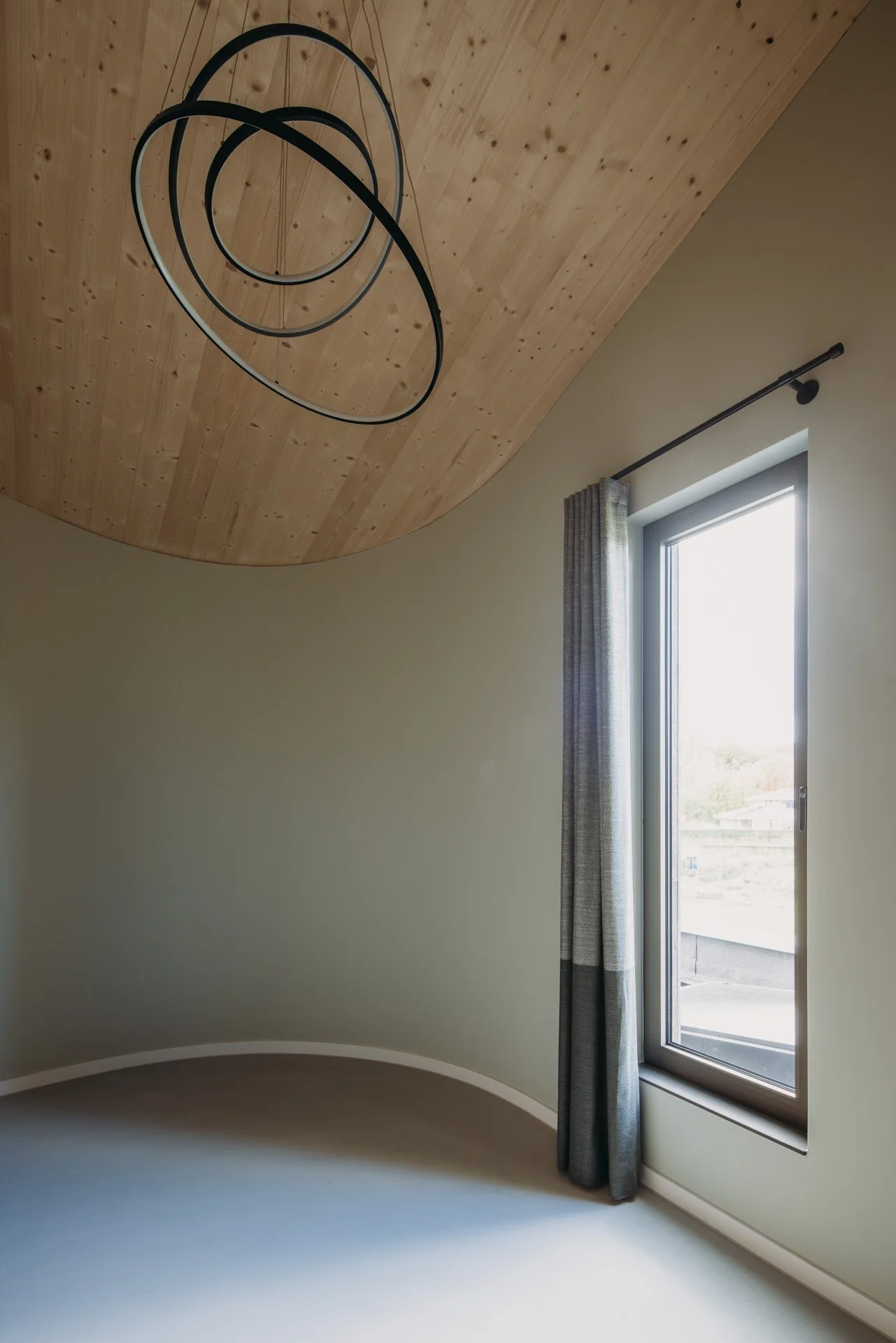 Kamer met schuin blank houten plafond, lichtgroene wanden en moderne spiraalvormige hanglamp.