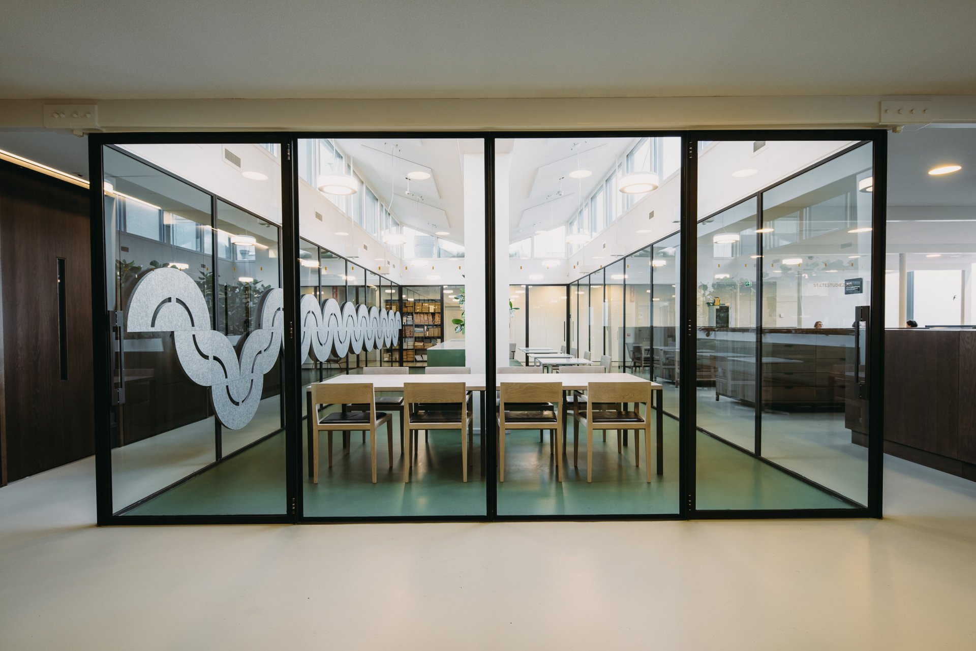 Overlegruimte met groene vloer, houten stoelen en witte tafel in atrium midden in open kantoorruimte