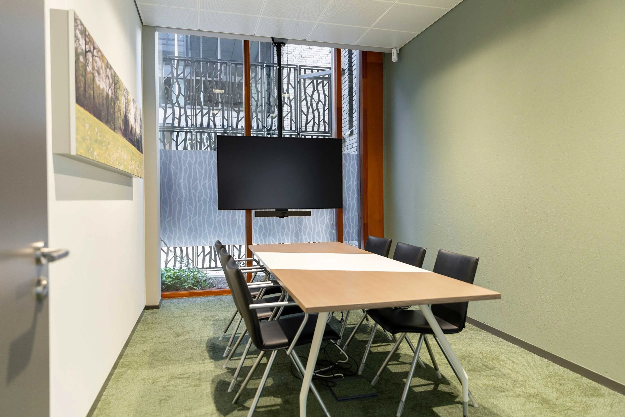 vergaderkamer met beeldscherm voor het raam en akoestisch paneel met fotoprint aan de wand.