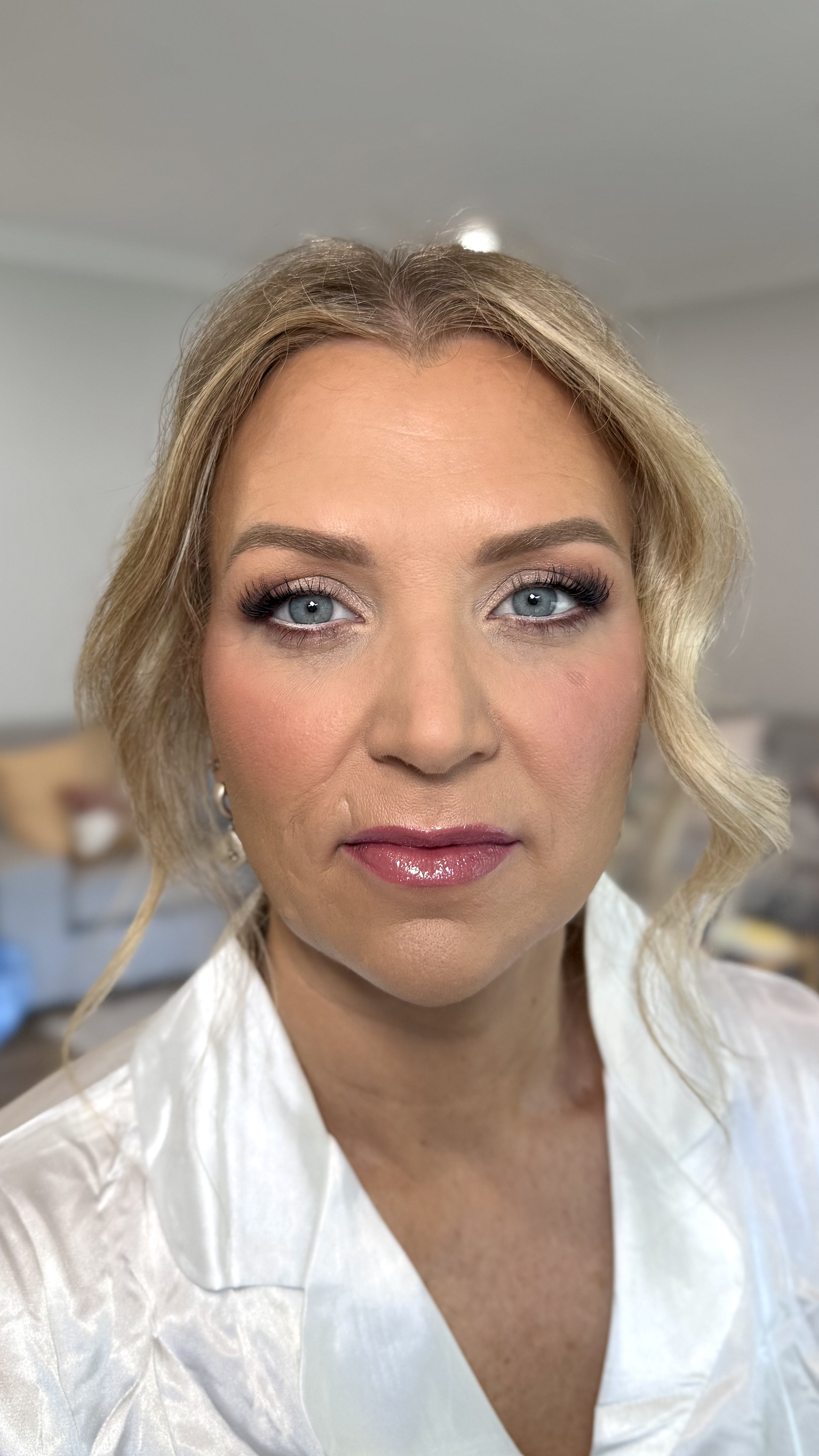 Close-up of a woman with blonde hair, blue eyes, makeup, and wearing a white satin shirt.