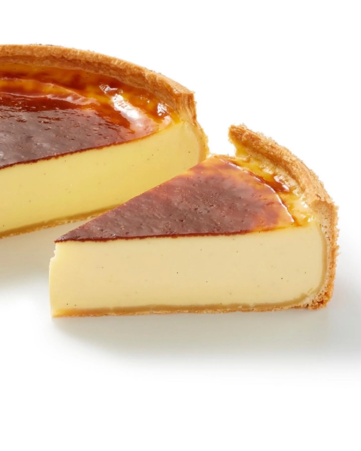 Gâteau au fromage avec une croûte dorée, une garniture caramel et une tranche coupée pour montrer la texture crémeuse à l'intérieur.