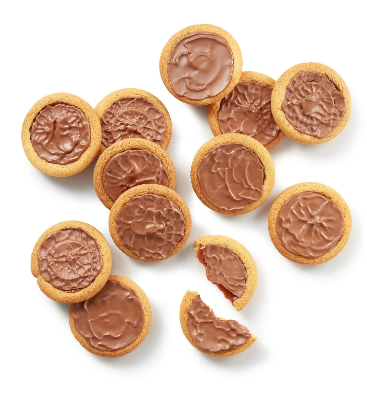 Biscuits ronds avec du chocolat au dessus disposés sur un fond blanc, dont un est cassé.
