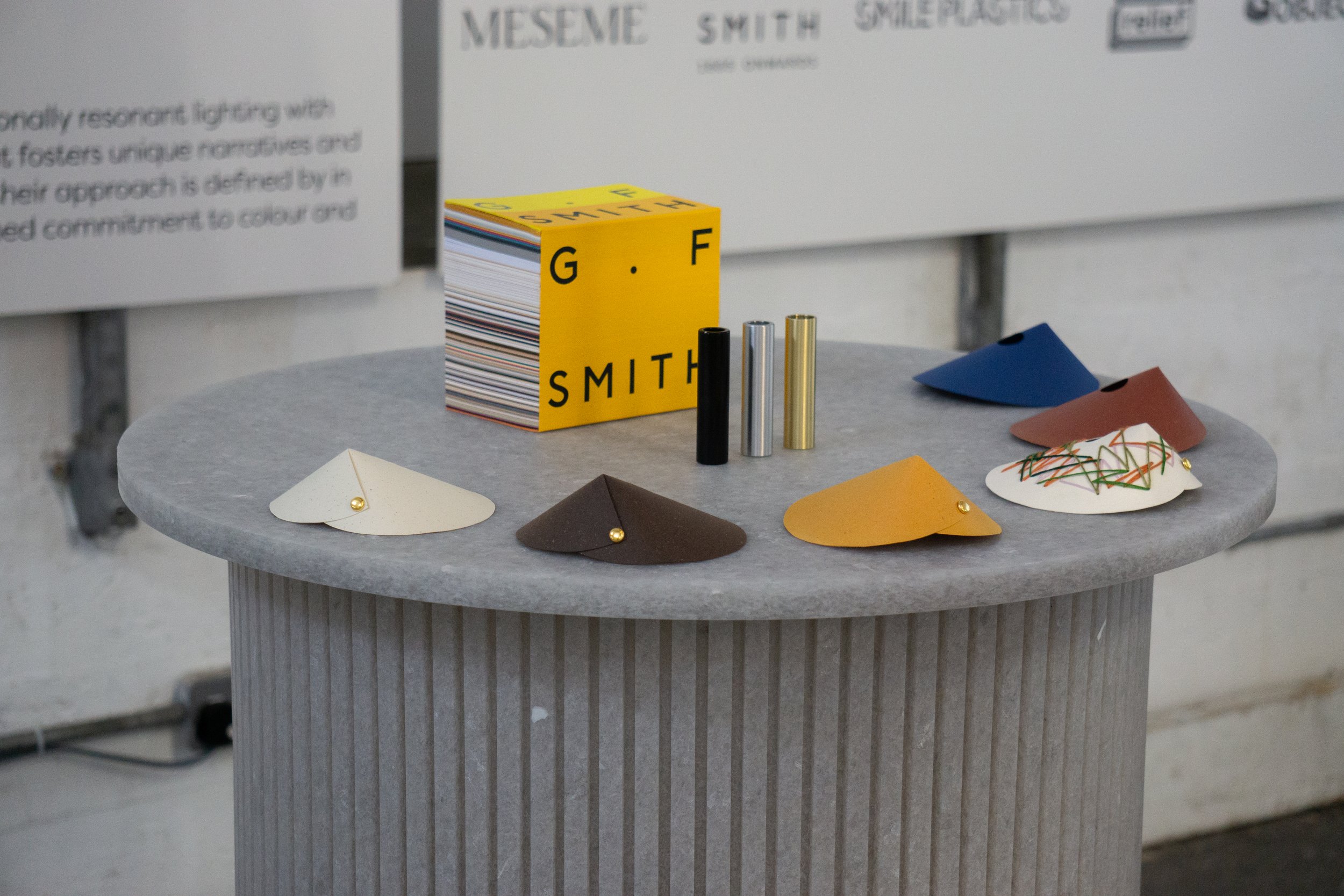 Assorted colored paper samples and materials on a round table with a G.F Smith swatch book.