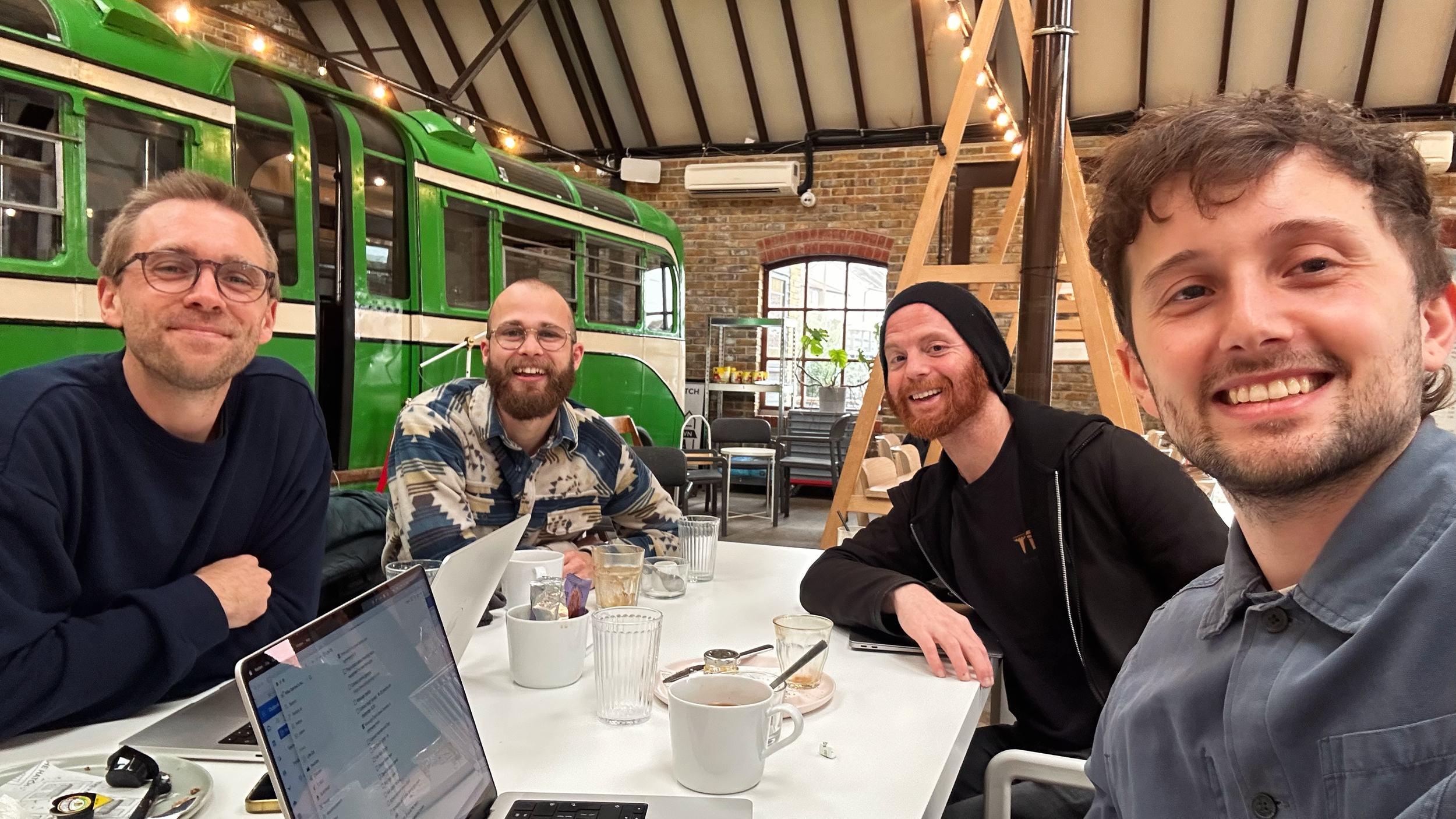 Four men from the music charity (TIME) sitting at a table in a cafe, pausing during their meeting to smile and pose for the photo.