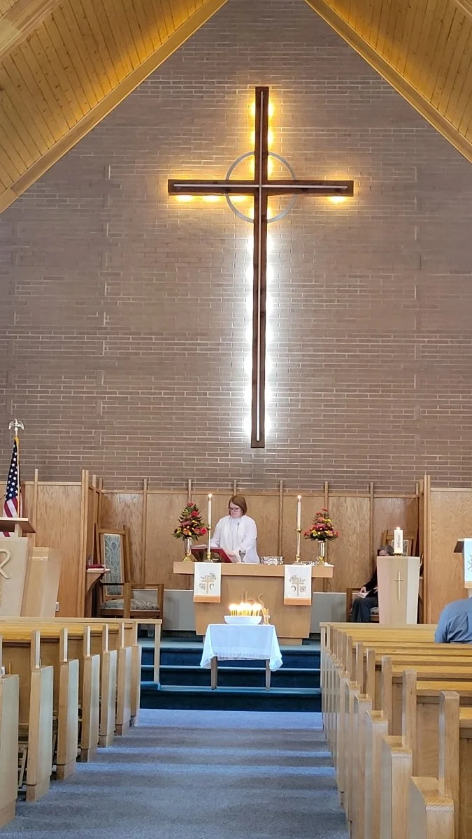 Clergy woman in sancturary with a cross behind heer