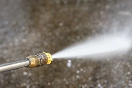 A pressure washer nozzle spraying water onto a concrete surface.