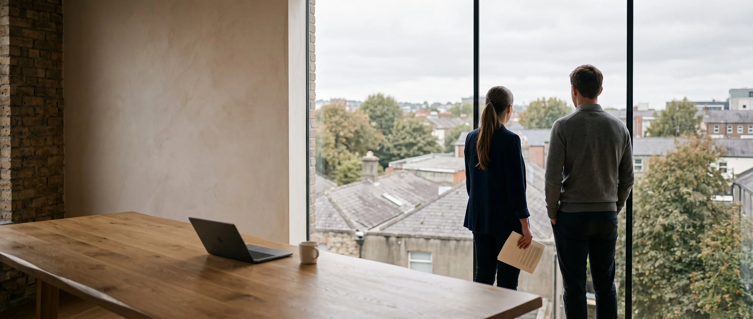 Two colleagues looking out over rooftops from an upper-floor meeting room
