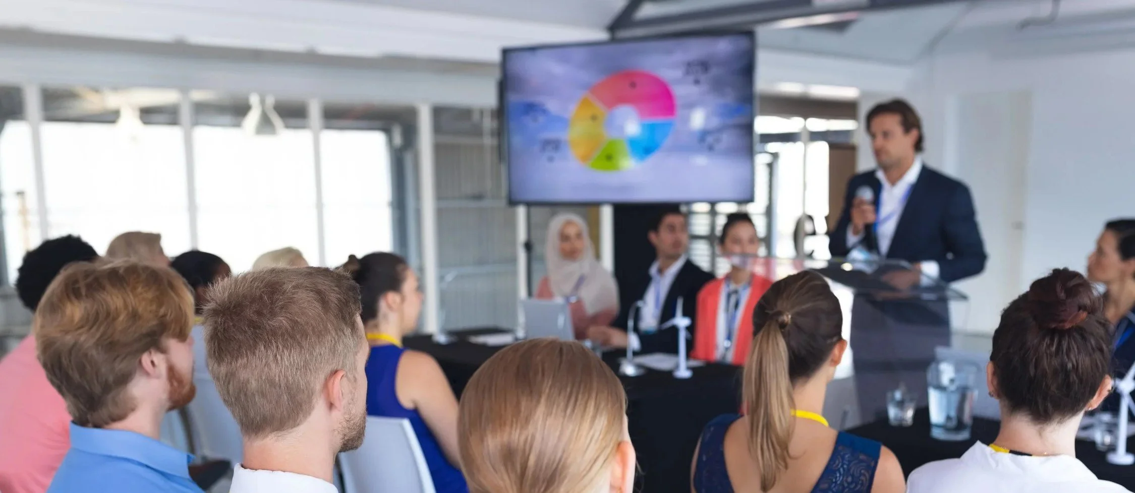 A speaker addressing a seated audience at a business conference