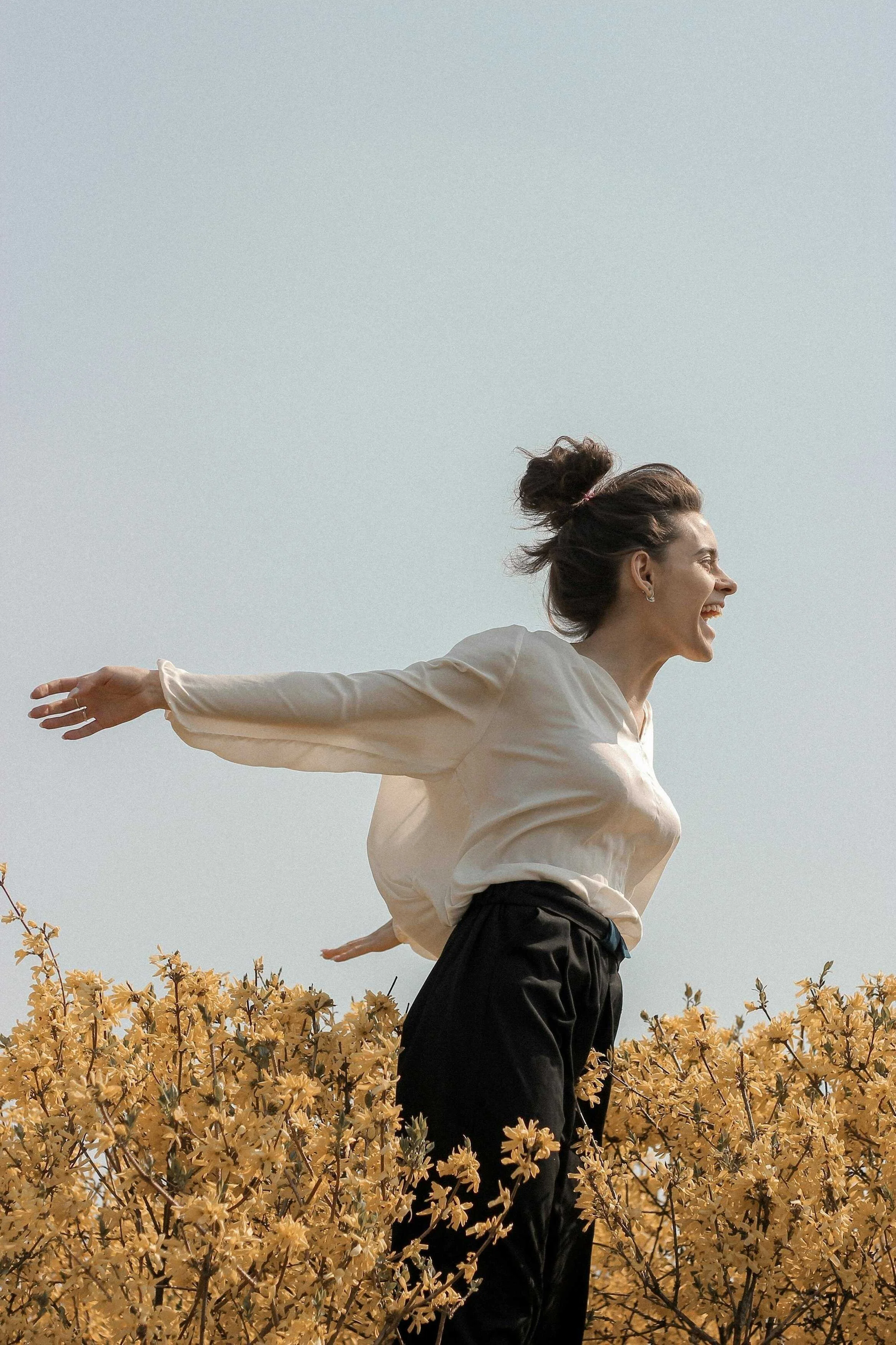 woman standing in a field with her arms open wide with yellow flowers celebrating life with therapy and support