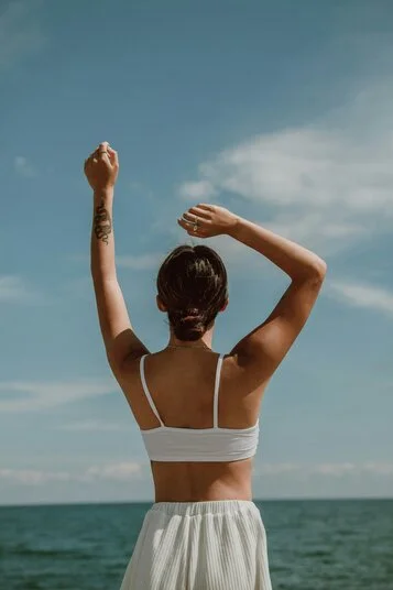 woman preparing for therapy stretching her arms into the blue sky by the ocean
