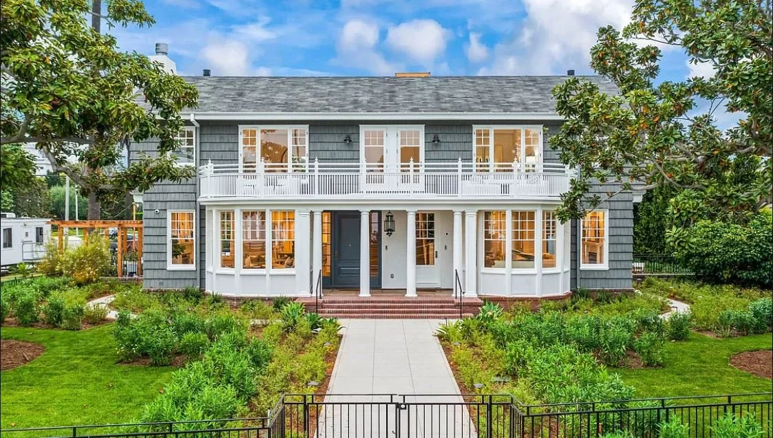 Two-story gray house with white trim, large windows, balcony, and garden