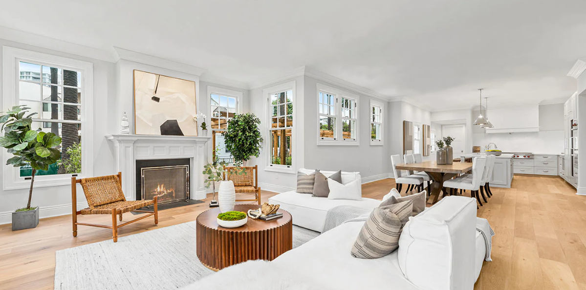Bright open-plan living and dining room with modern decor, featuring a fireplace, large windows, white walls, wooden floor, and contemporary furniture including sofas, a dining table, and chairs.