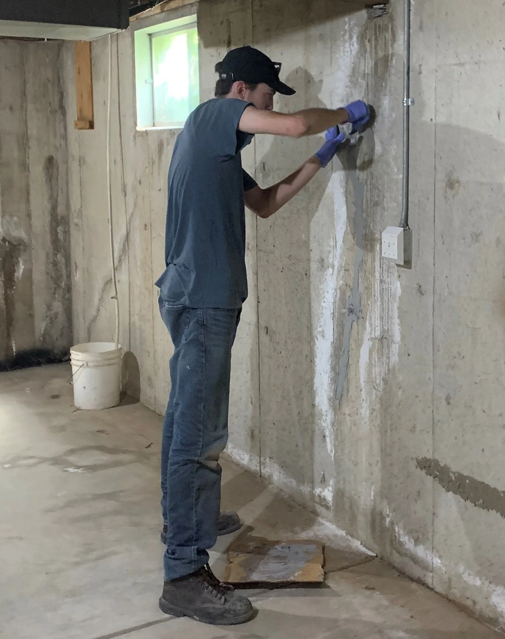 A crack attack technician repairing a vertical crack in a concrete foundation wall.