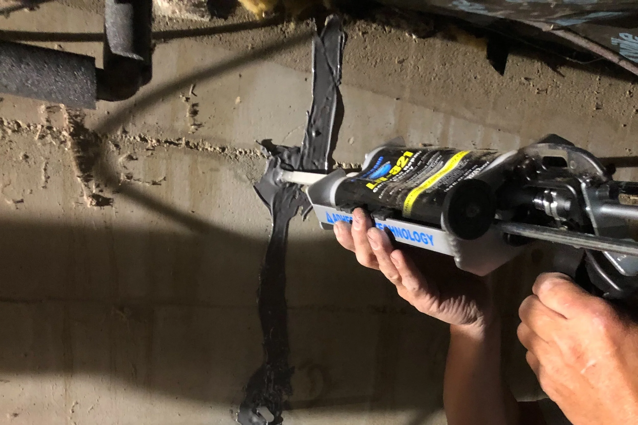 A technician injecting low-viscosity epoxy into a small vertical concrete foundation wall crack.