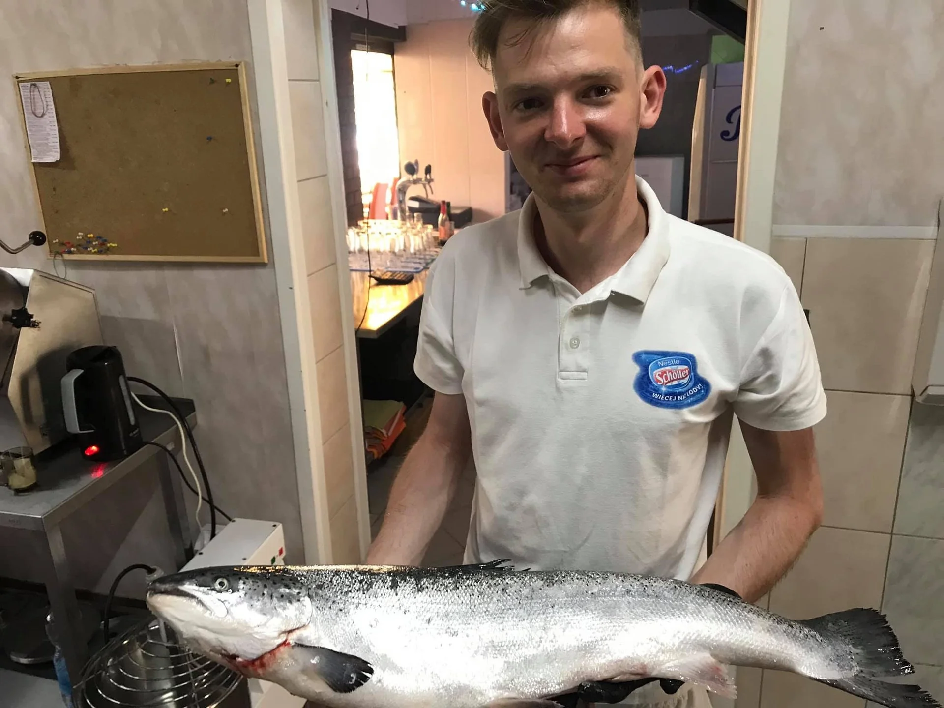 A man holding a large fish in a kitchen setting.