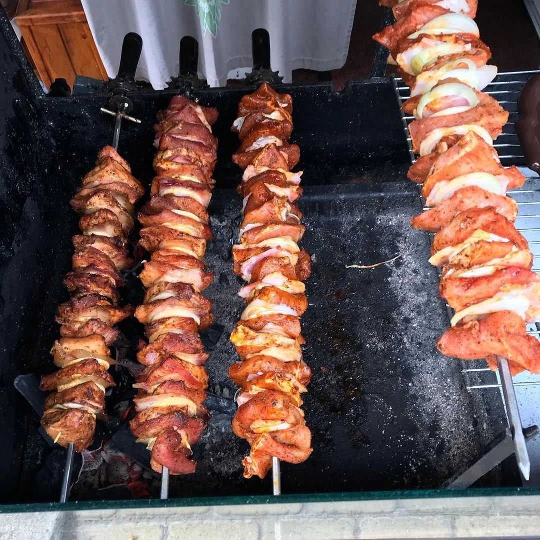 Three skewers of grilled meat, possibly chicken or pork, with slices of onion, on a black griddle, with additional skewers on the side.
